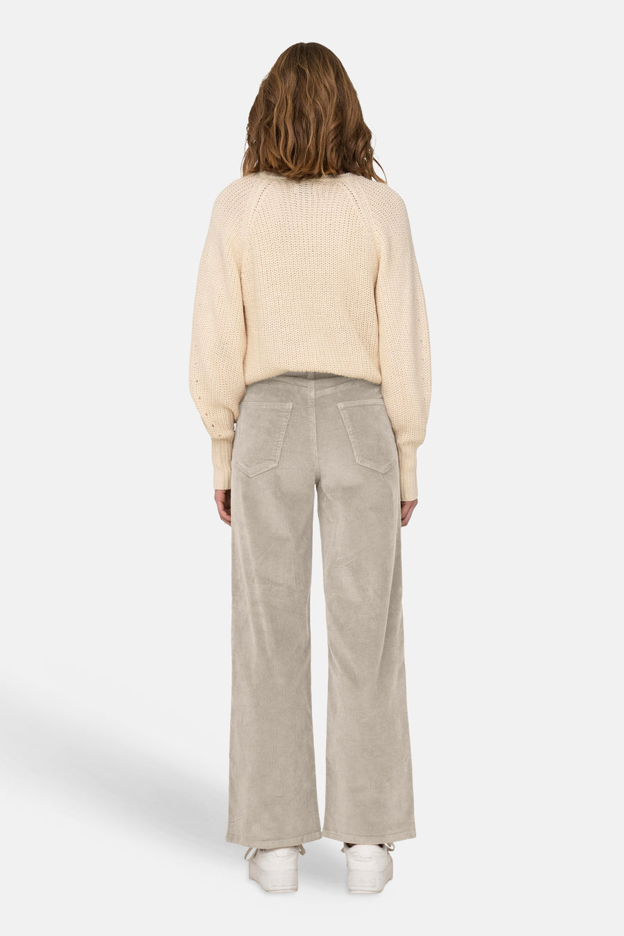 Pantalon couleur velours côtelé oatmeal de ONLY®, dos avec poches, jambes larges, modèle portant un pull crème et des baskets blanches