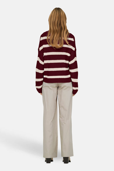 Rode trui met ronde hals van JDY met witte strepen, gedragen met een beige broek.
