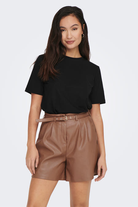 T-shirt noir ONLY, manches courtes, combiné avec des shorts en cuir brun et des bottes noires.