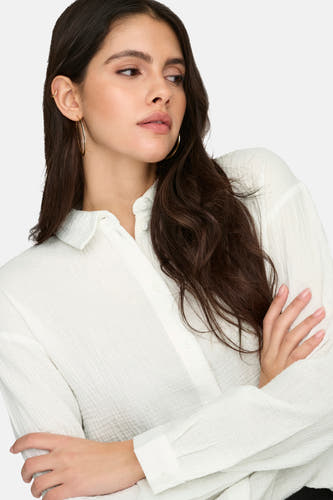 Chemise blanche à manches longues de JDY, avec une texture subtile et les bras croisés.