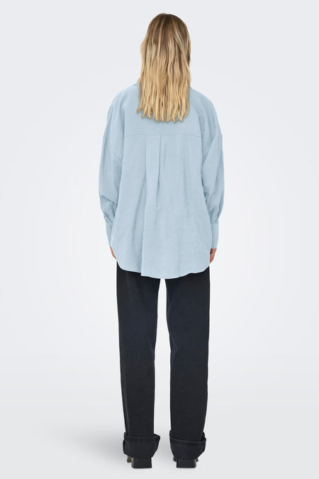 Chemise bleue à manches longues ONLY, avec des plis dans le dos et portée avec un jean noir.