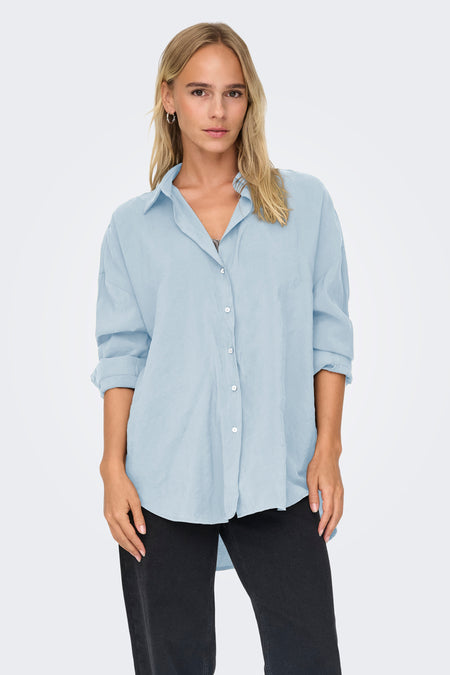Chemise bleue à manches longues ONLY, coupe décontractée portée avec un jean noir et des boucles d'oreilles argentées.