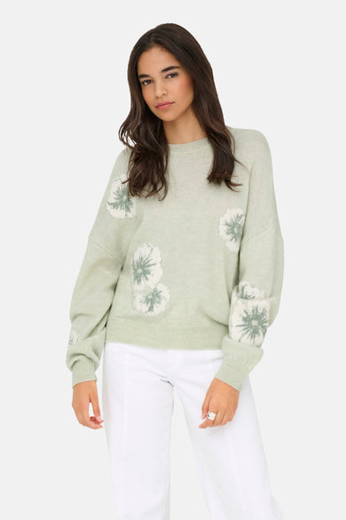 Pull vert avec col rond de JDY, avec détails de fleurs blanches sur le devant et les manches, combiné avec un pantalon blanc.