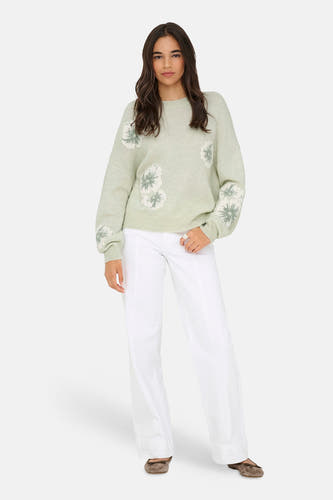 Groene trui met ronde hals van JDY, met witte bloemendetails op de voorkant en mouwen, gecombineerd met een witte broek.

