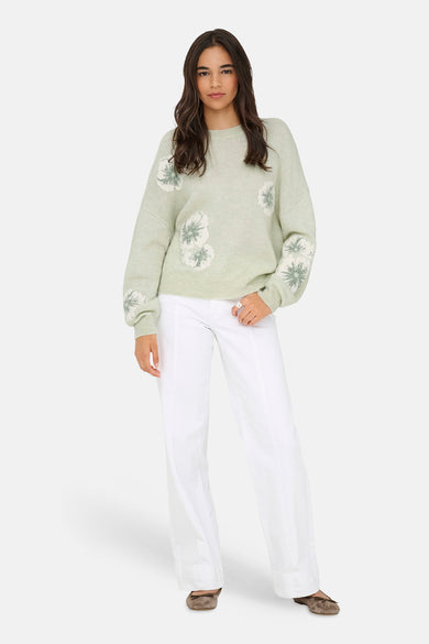 Groene trui met ronde hals van JDY, met witte bloemendetails op de voorkant en mouwen, gecombineerd met een witte broek.
