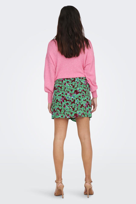 Korte groene rok van ONLY, met bloemmotief, gecombineerd met een roze trui en beige hakken, gezien van achteren.
