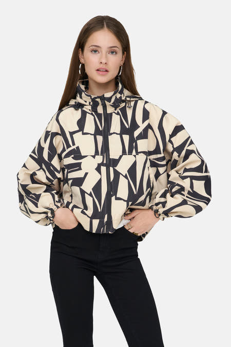 Manteau court beige d'ONLY avec un motif abstrait noir, porté avec un pantalon noir et des bottes.