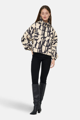 Beige korte jas van ONLY met een abstract zwart patroon, gedragen met zwarte broek en laarzen.