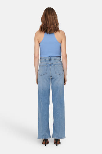 Jean bleu clair large d'ONLY, avec une taille haute et porté avec un haut bleu et des baskets noires.