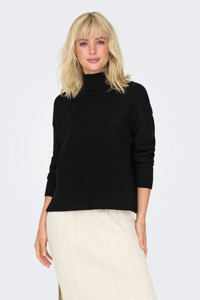Pull noir avec col montant d'ONLY, associé à une jupe crème cotonnée avec fente et des bottes noires.