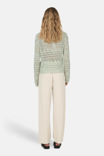 Pull ajour vert avec col rond de JDY, avec ourlet festonné, porté avec un pantalon clair et des sandales noires, vu de dos.