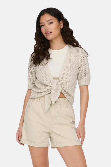 Veste beige de JDY, boutonnée à l'avant, portée sur un t-shirt blanc avec des pantalons courts coordonnés et des baskets.