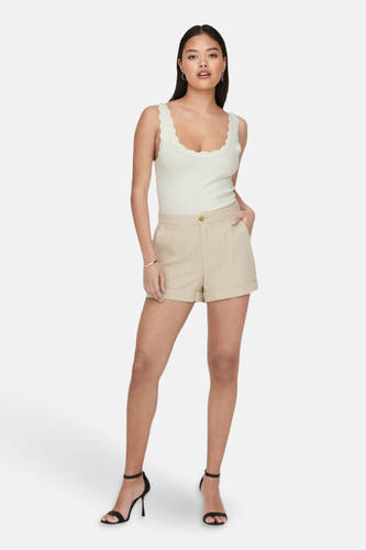 Haut blanche sans manches de JDY avec bord festonné et tissu côtelé, portée avec un short beige et des talons noirs.