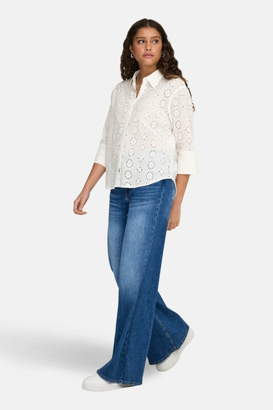 Chemise blanche à manches longues de JDY, avec détails brodés et portée avec un jean bleu foncé et des baskets blanches.