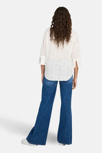 Chemise blanche à manches longues de JDY, avec détails ajourés, portée avec un jean bleu.