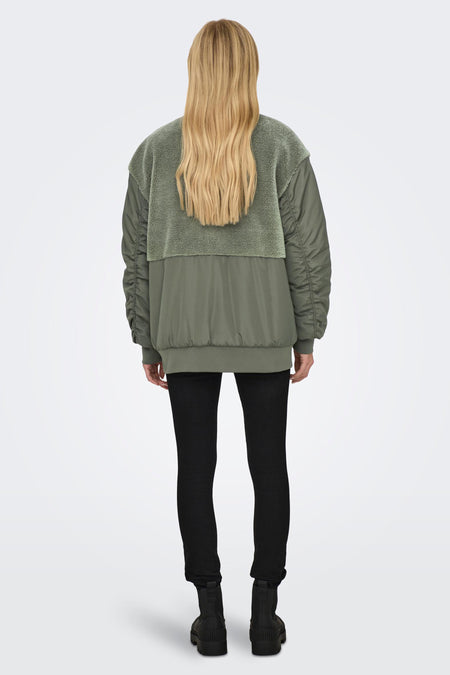 Veste verte ONLY, avec un col en teddy et des manches froncées, associée à un pantalon noir et des bottes.