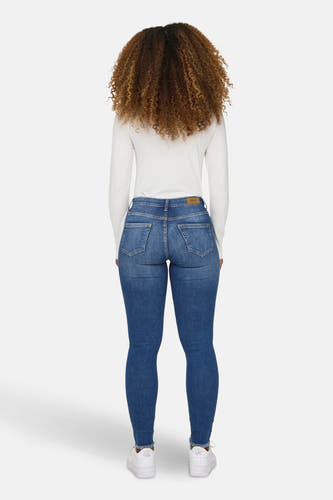 Jean skinny bleu ONLY, avec un t-shirt blanc à longues manches et des baskets blanches.