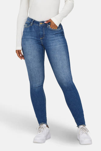 Blauwe skinny jeans van ONLY, met een hand in de zak en gedragen met een wit shirt.
