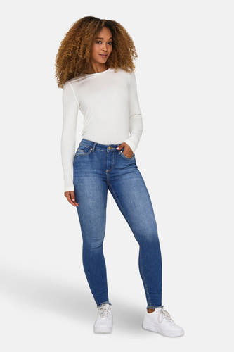 Skinny jeans van spijkerstof in blauw, de 'BLUSH SKINNY' van ONLY, met een dame in witte top en schoenen.

