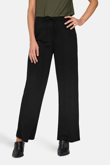 Pantalon noir de ONLY, avec cordon, porté avec un chemisier vert et des chaussures noires.