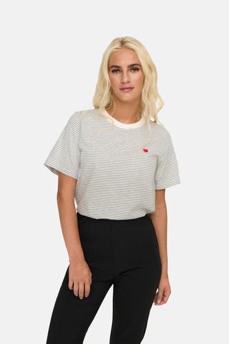 T-shirt gris rayé à manches courtes de JDY, avec une petite application de cœur rouge. La dame porte un pantalon noir.