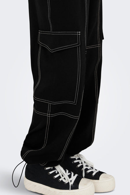 Pantalon cargo noir ONLY, avec des surpiqures et poches blanches, associé à des sneakers noires avec l lacets.