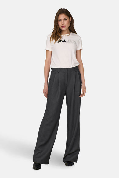 Pantalon gris de costume ONLY, avec plis et larges pinces, associé à un T-shirt blanc et une chaîne dorée.