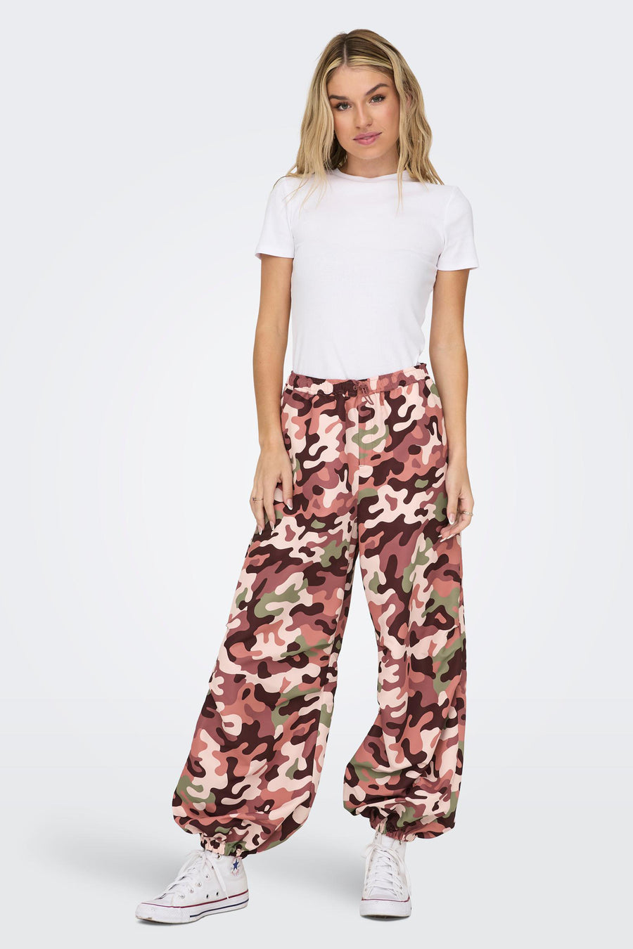 Pantalon camouflage de NEON & NYLON, avec une ceinture élastique et des jambes larges, associé à des chaussettes blanches et un t-shirt blanc.