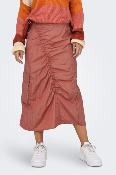 Robe rose de NEON & NYLON, avec détail drapé et poche cargo, associée à un pull rayé et des baskets blanches.