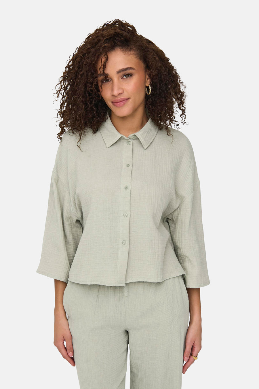 Chemise verte à manches courtes de JDY, avec une texture froissée et des boucles d'oreilles dorées.