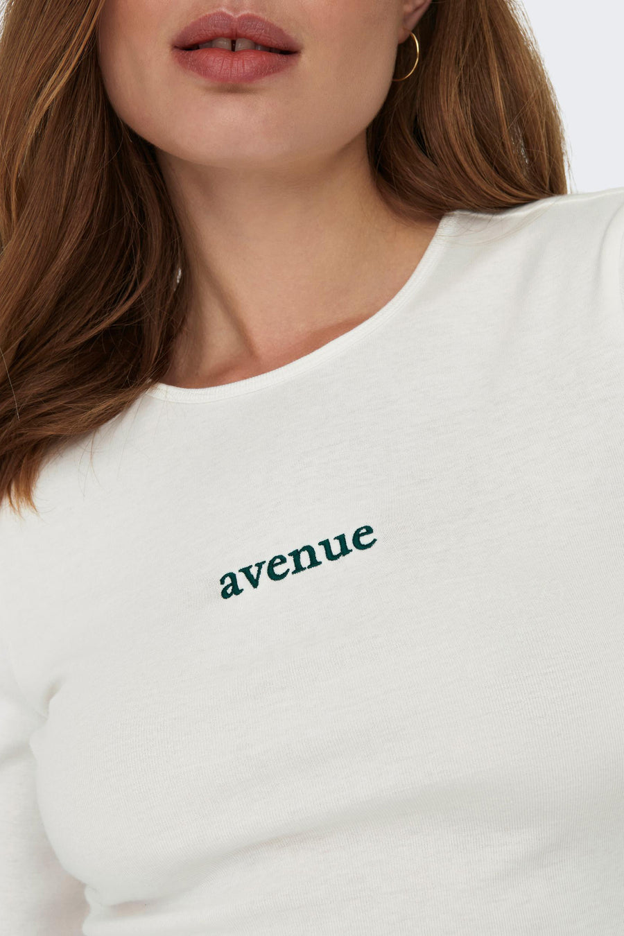 T-shirt blanc à manches longues de ONLY, avec le texte 'avenue' imprimé dessus et des boucles d'oreilles en or.