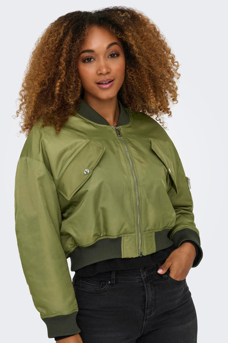 Veste courte verte de ONLY, avec des poches et une fermeture éclair argentée, portée avec un pantalon noir.