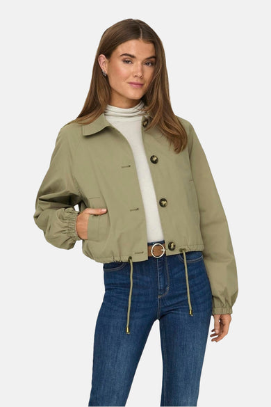 Manteau court vert de ONLY, avec fermeture à boutons, longues manches et une veste beige et des jeans bleus.