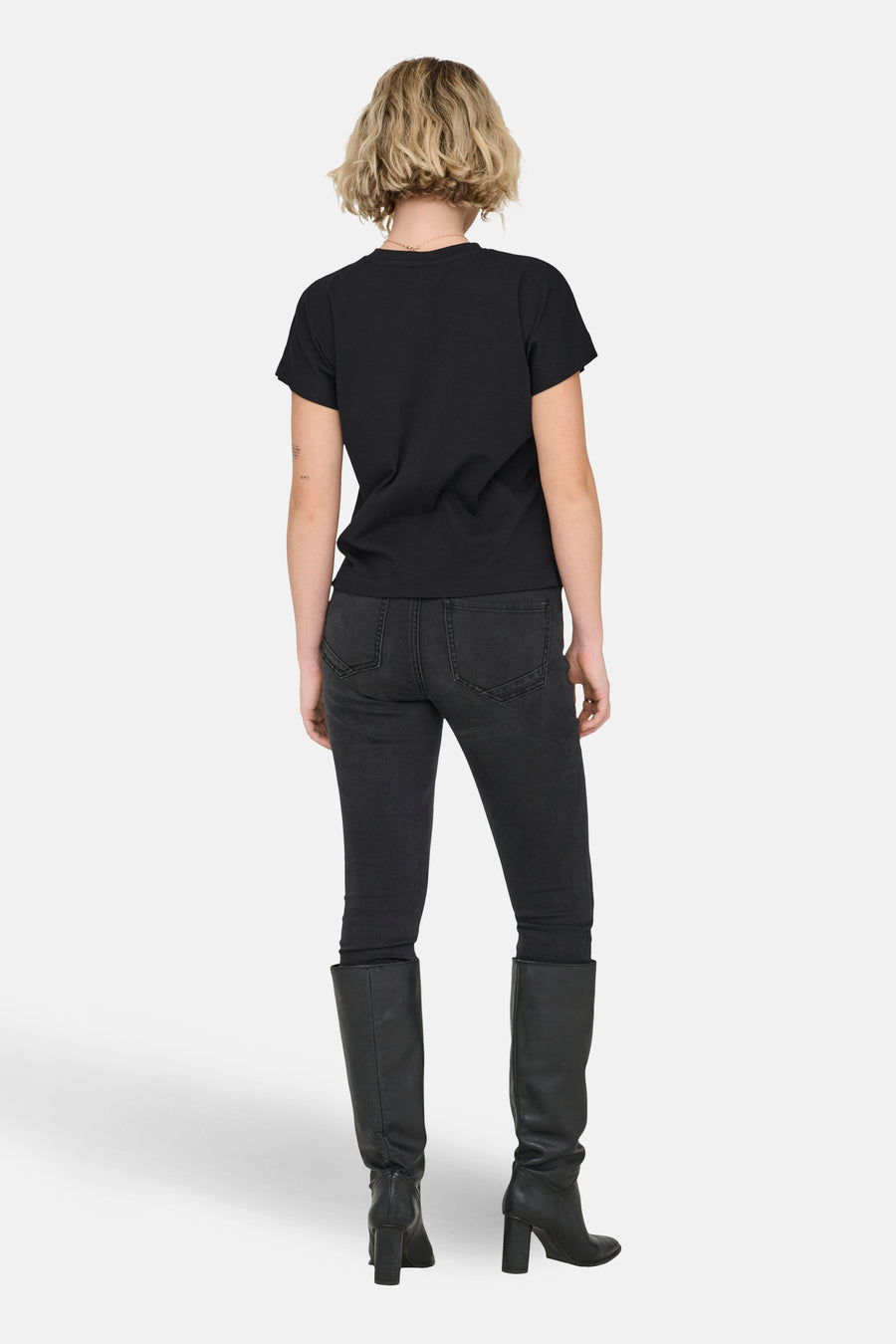 T-shirt noir à manches courtes ONLY®, vu de dos, combiné avec un jean noir et des bottes en cuir à talons.