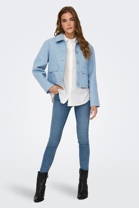 Blauwe korte jas van JDY, met knoopsluiting, opgestikte zakken en gecombineerd met een witte blouse en blauwe jeans.
