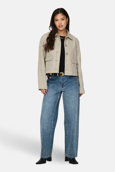 Manteau court beige de JDY, avec des manches longues et une fermeture à boutons, associé à un haut noir et des jeans bleus.