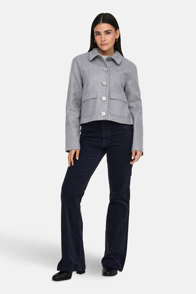 Manteau court gris de JDY, avec des boutons, des poches et associé à un pantalon corduroy bleu marine.