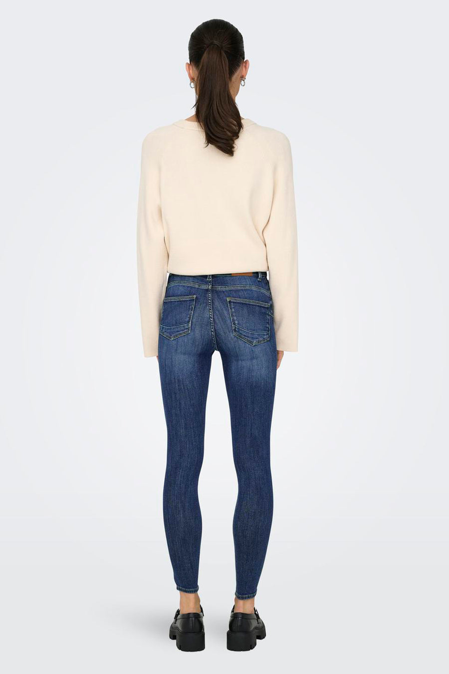 Donkerblauwe skinny jeans van denim van ONLY®, achterkant, gedragen met een lichte trui en zwarte schoenen.
