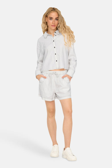 Witte short van ONLY, met trekkoord en zwarte stiksels, gedragen met een bijpassende blouse en witte sneakers.
