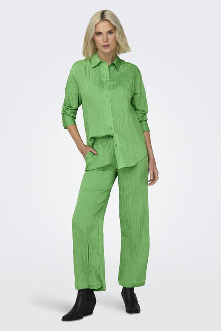 Pantalon vert de ONLY avec une texture froissée, associé à un chemisier vert coordonné et des chaussures noires.