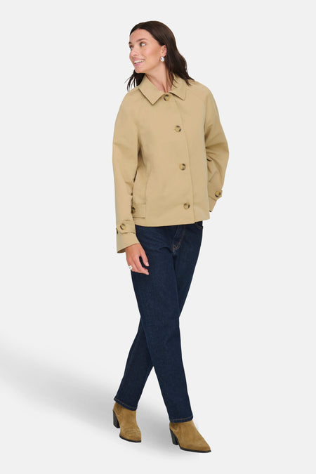 Vrouw in beige jas, spijkerbroek en suède laarzen.