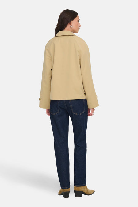 Dame, rug, beige jas, donkere jeans, suède laarzen.