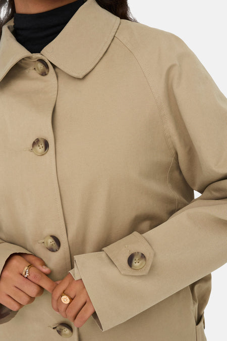Beige trenchcoat met knopen en gouden ringen.
