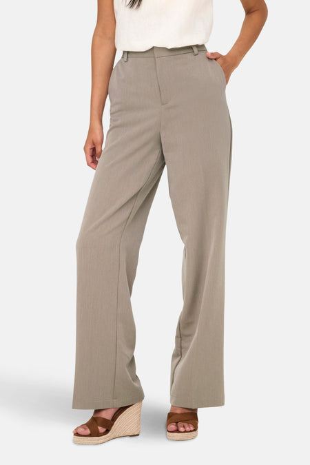 Vrouw in grijze pantalon met wijde pijpen en bruine sleehakken.