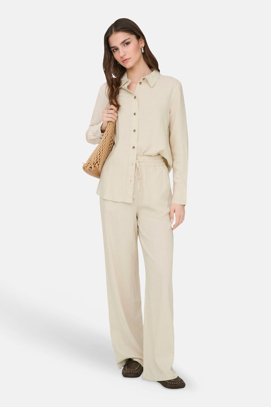 Beige broek van JDY met een subtiele textuur, wijde pijpen en trekkoord, gecombineerd met een bijpassende blouse en rieten tas.