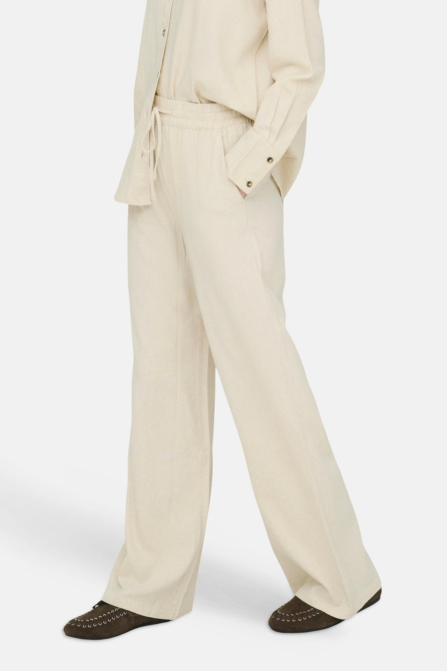 Pantalon beige de JDY, en tissu aspect lin, avec taille élastique, cordon de serrage et jambes larges, porté avec une chemise assortie.