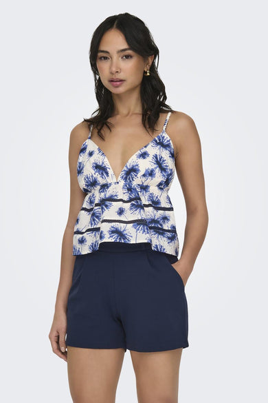 Blouse blanche sans manches à imprimé floral bleu avec volants de la marque ONLY®, portée avec un short bleu marine, vue de face
