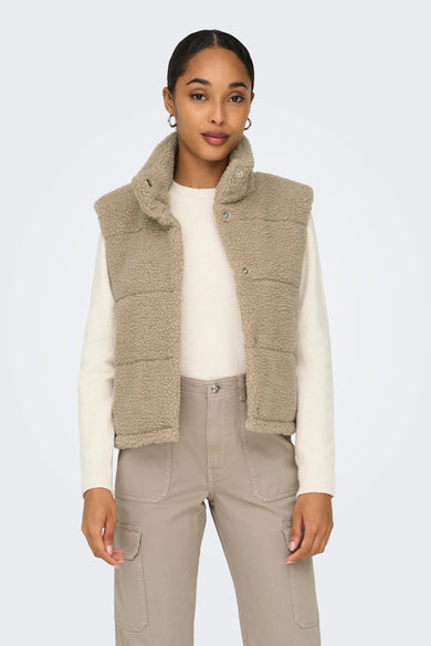 Doudoune sans manches beige imitation fourrure de ONLY® avec boutons, col montant et poches, portée sur un pull blanc et un pantalon beige