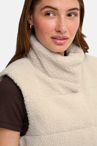 Doudoune sans manches couleur crème en tissu de peau de mouton avec col montant, de la marque ONLY®, portée sur un pull côtelé marron foncé, gros plan de l'avant