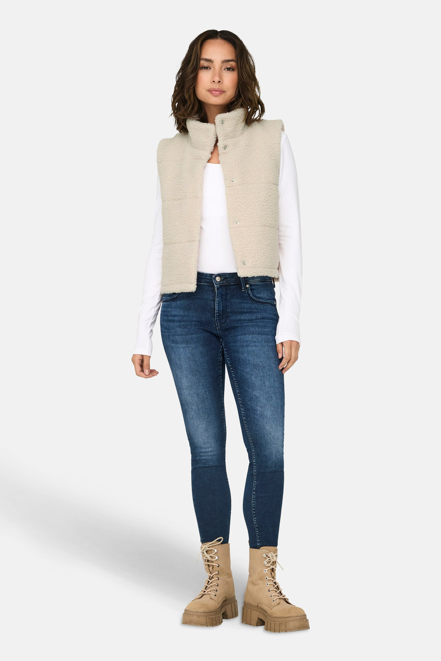 Gilet écru de ONLY, porté sur un t-shirt blanc à manches longues et des jeans foncés, associé à des bottes beige.